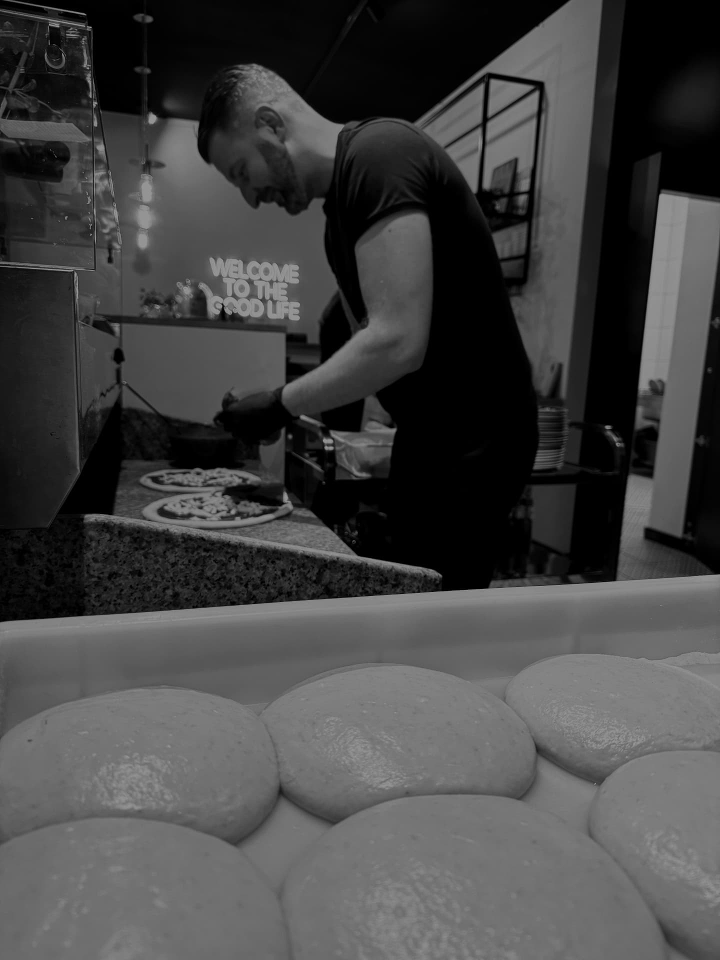 Pizzaiolo FUMO przygotowuje pizzę przy blacie, z ciastem na pierwszym planie