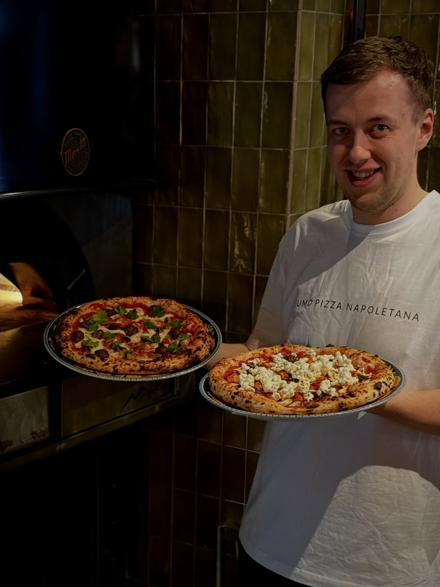 Pizzaiolo przy piecu z dwiema pizzami